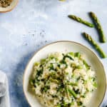 Overhead shot of a single bowl with wild garlic and asparagus risotto with few asparagus tips and lemons on side