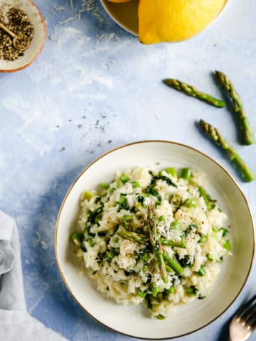 Overhead shot of a single bowl with wild garlic and asparagus risotto with few asparagus tips and lemons on side