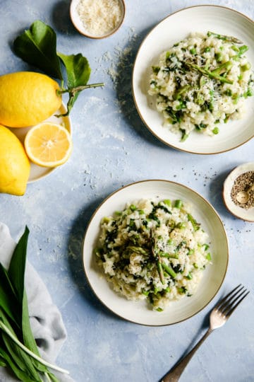 overhead shot of two bowls with wild garlic and asparagus risotto with some lemons on side