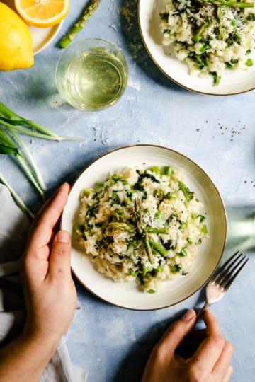 overhead shot of person holding a bowl with wild garlic and asparagus risotto