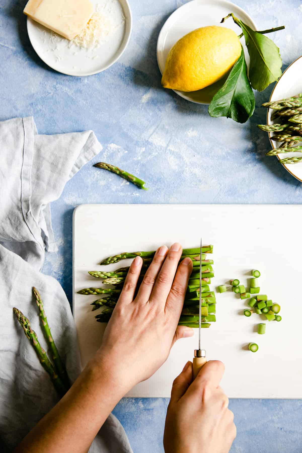 overhead shot of a person chopping the green asparagus on a white chopping board