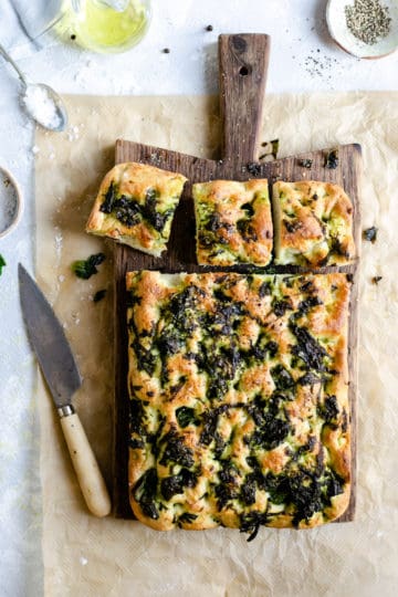 overhead shot of wild garlic and black pepper focaccia on a wooden chopping board