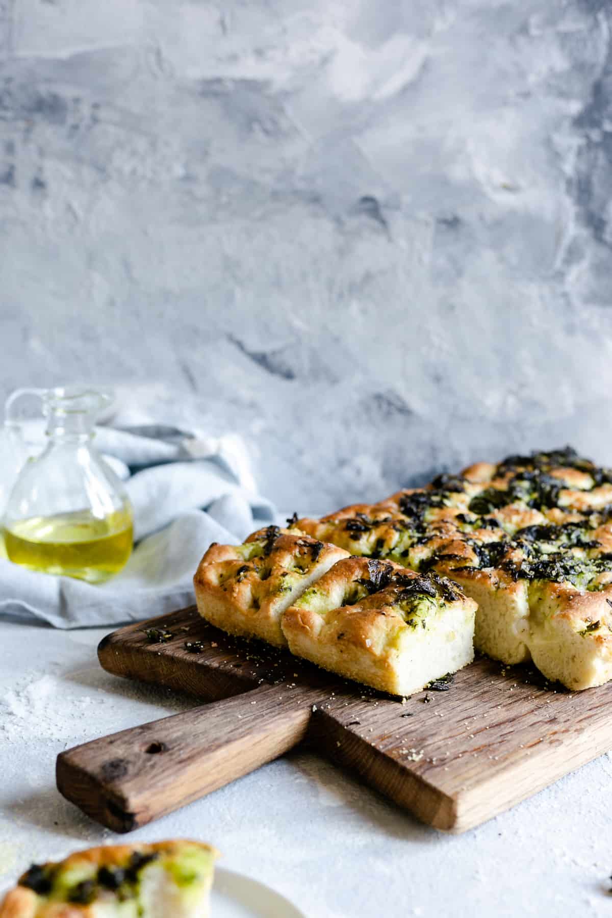 side angle shot of wild garlic and black pepper focaccia bread with small bottle of olive oil on side