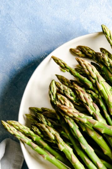 close up of green asparagus tips in a white plate on a blue backdrop