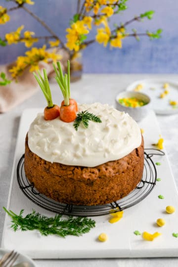 45 degree angle shot of the easy vegan carrot cake on a round metal cooling rack with some yellow flowers in the background
