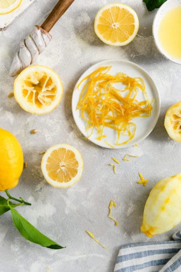 overhead shot of candied lemon peel in a small plate, surrounded by lemon halves and whole lemons
