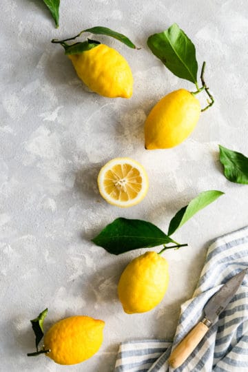 overhead shot of four whole lemons with leaves and one half of lemon sliced