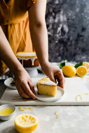 a side angle shot of a person holding a small plate with a slice of lemon cake