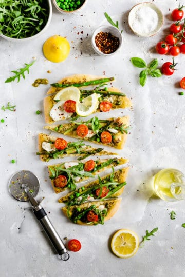 overhead shot of sliced rocket and asparagus pizza topped with cherry tomatoes