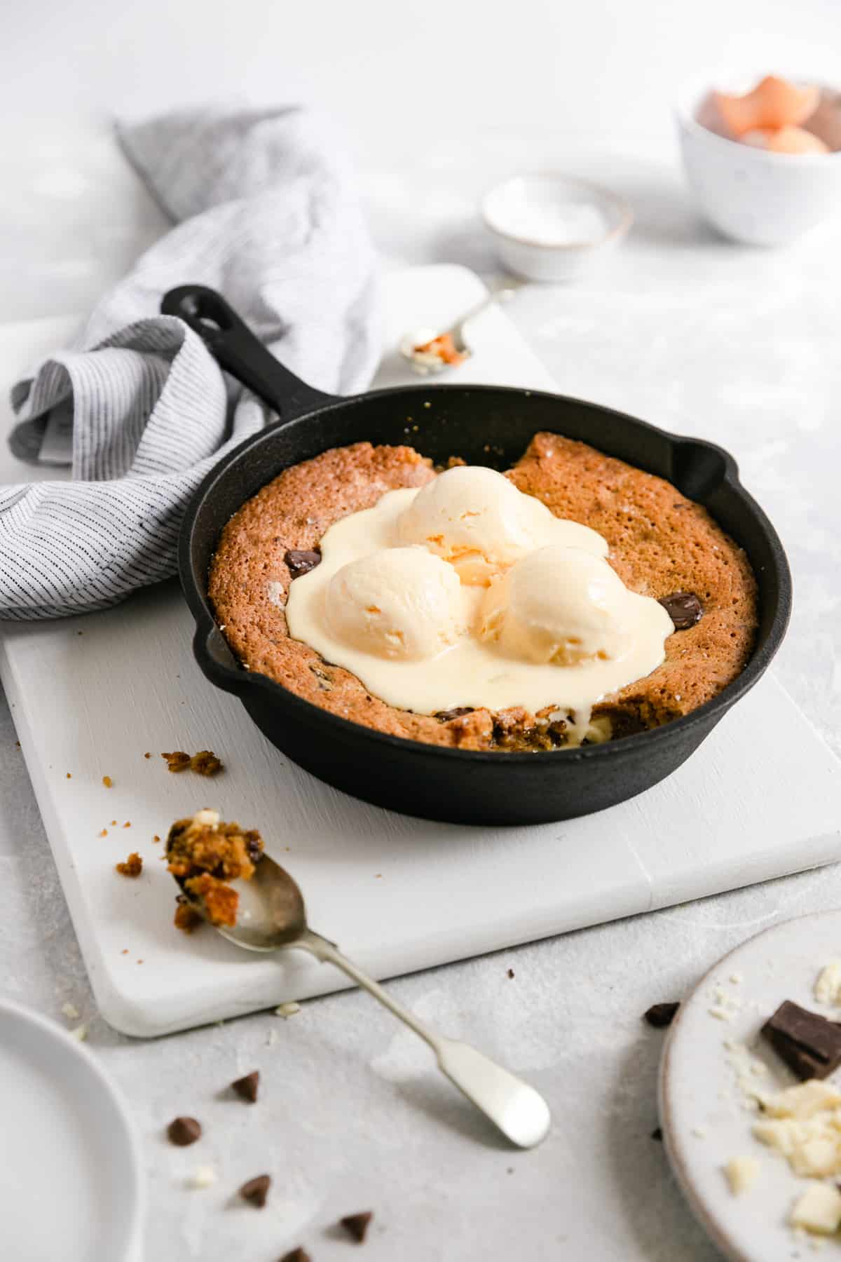 a side shot of a skillet with chocolate chip and malted milk cookie inside topped with vanilla ice cream
