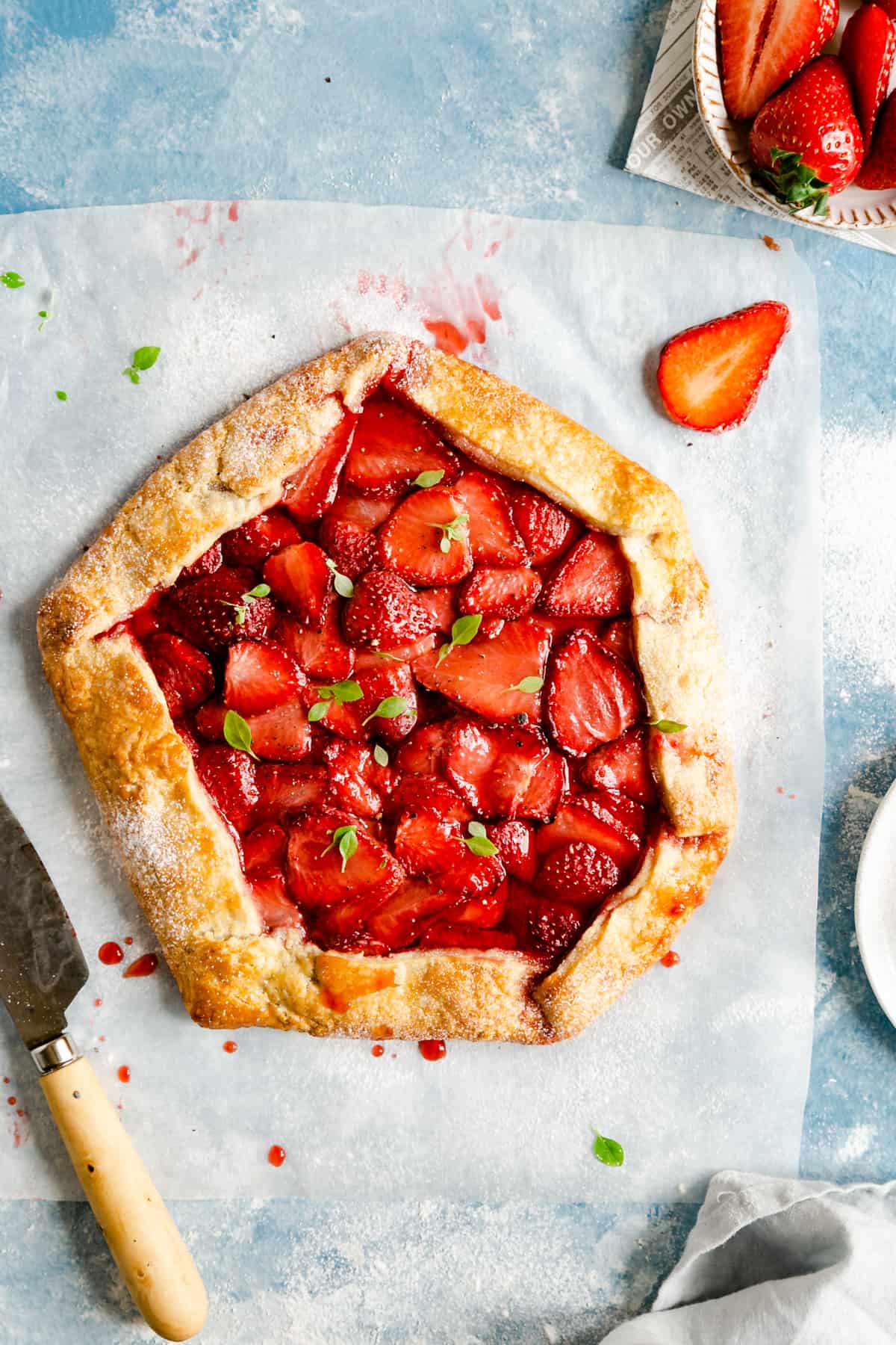 overhead shot of baked strawberry galette with basil leaves scattered on top