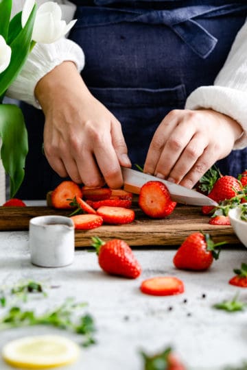 a close up of a person's hands slicing strawberries on a wooden chopping board