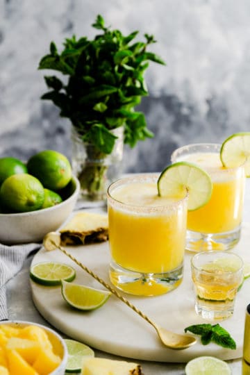two glasses with pineapple margaritas on a marble chopping board