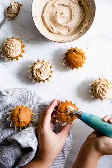 a person piping chai frosting on top of pumpkin cupcakes