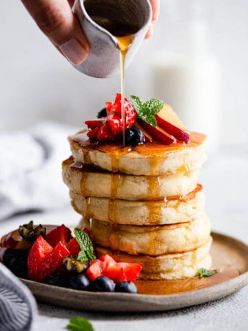 maple syrup being poured over fluffy pancakes.