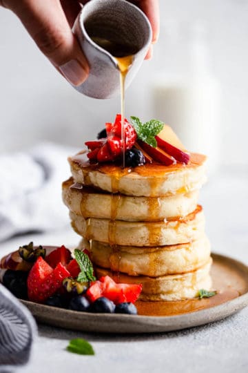 maple syrup being poured over fluffy pancakes.