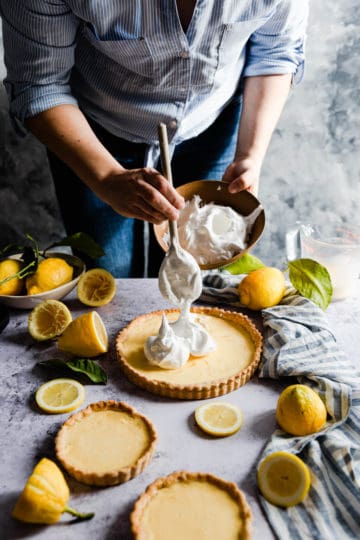 side shot of a person topping the lemon pie with meringue