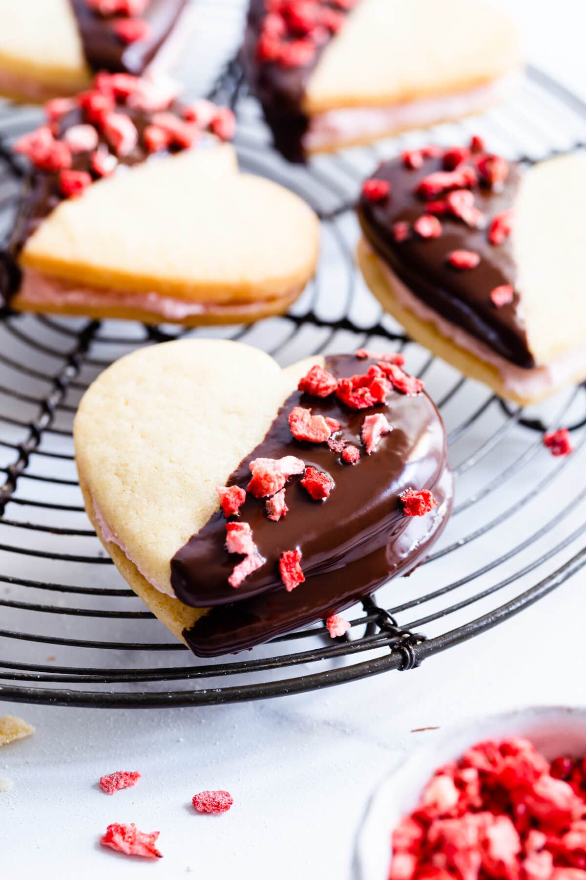 heart sandwich cookie topped with freeze dried strawberries on a cooling rack.