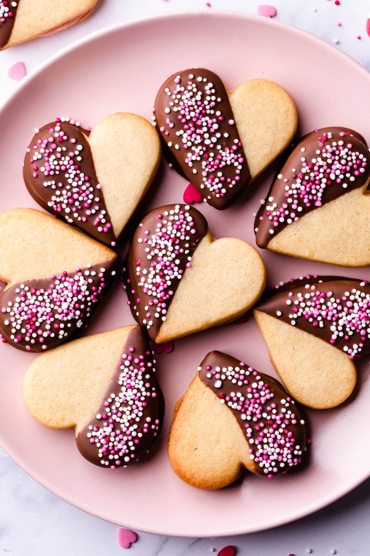 valentine sugar cookies topped with pink and white sprinkles on a pink plate.