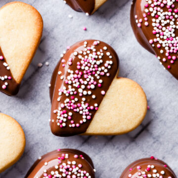 heart sugar cookie dipped in chocolate and topped with pink and white sprinkles.