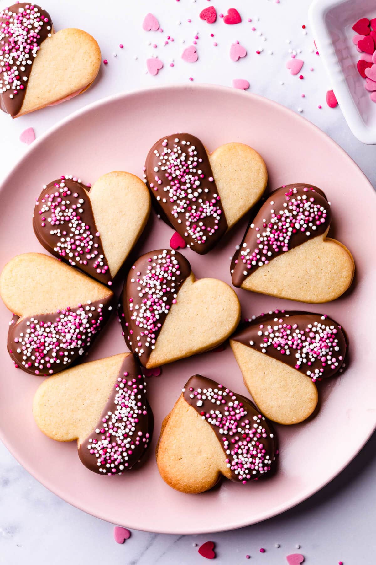 pink plate with valentine sugar cookies covered in chocolate and sprinkles.