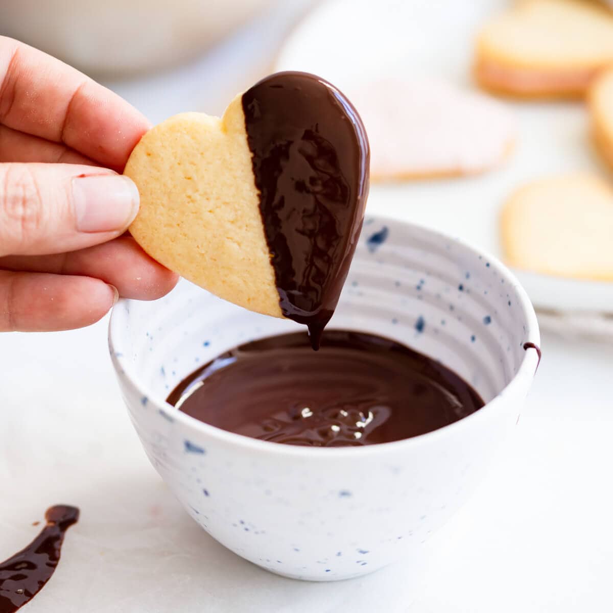 heart-shaped sugar cookie being dipped in melted chocolate.