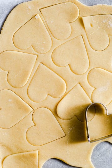 close up shot at cookie dough with heart shapes being cut out of it