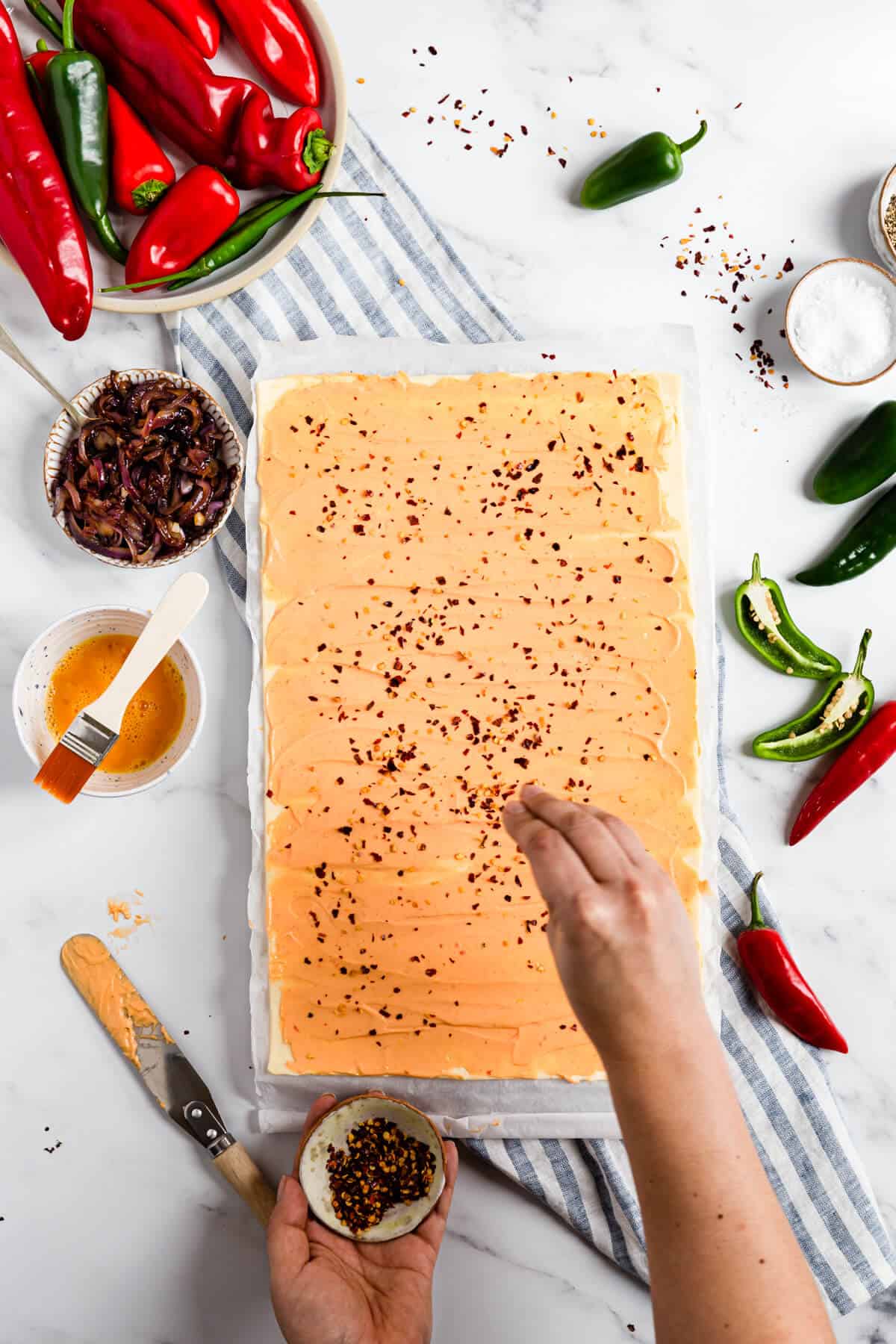 overhead shot of a person sprinkling chilli flakes over puff pastry with cheese
