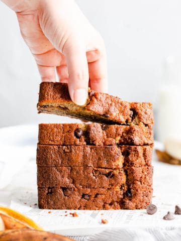 straight-ahead shot of a person taking a slice of banana bread from a stack of slices