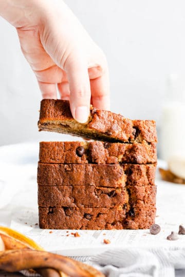 straight-ahead shot of a person taking a slice of banana bread from a stack of slices