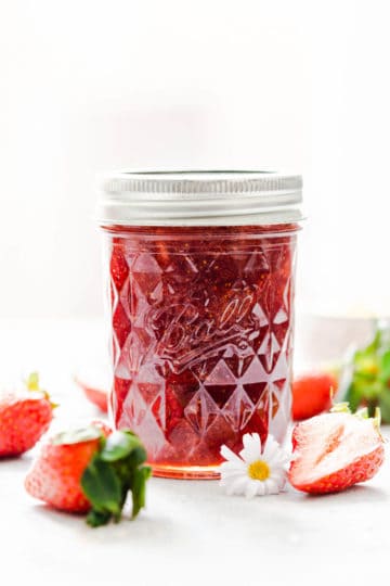 straight ahead shot at a jar with strawberry jam and some strawberries around it