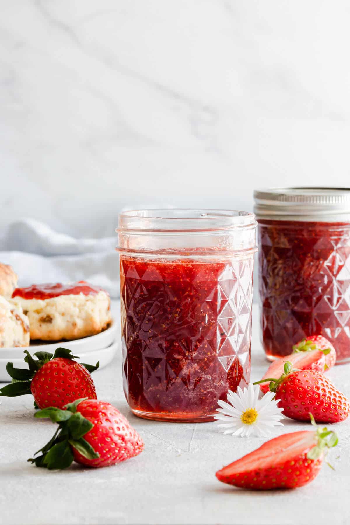 straight ahead shot of glass jar with jam inside and fresh strawberries around it