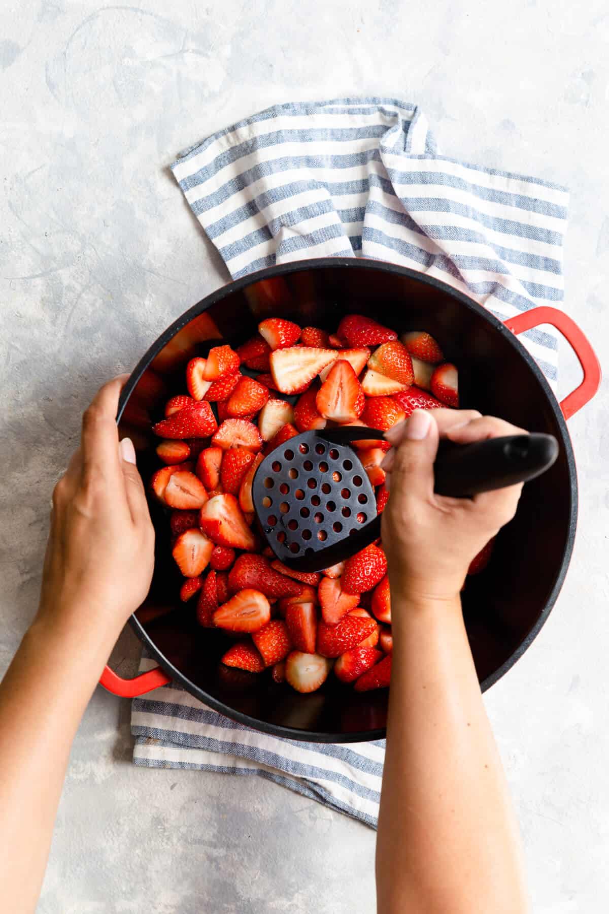 top view of a person crushing strawberries with potato masher