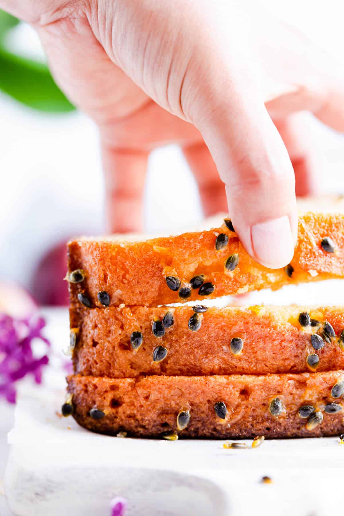 super close up of a hand lifting a slice of passion fruit loaf