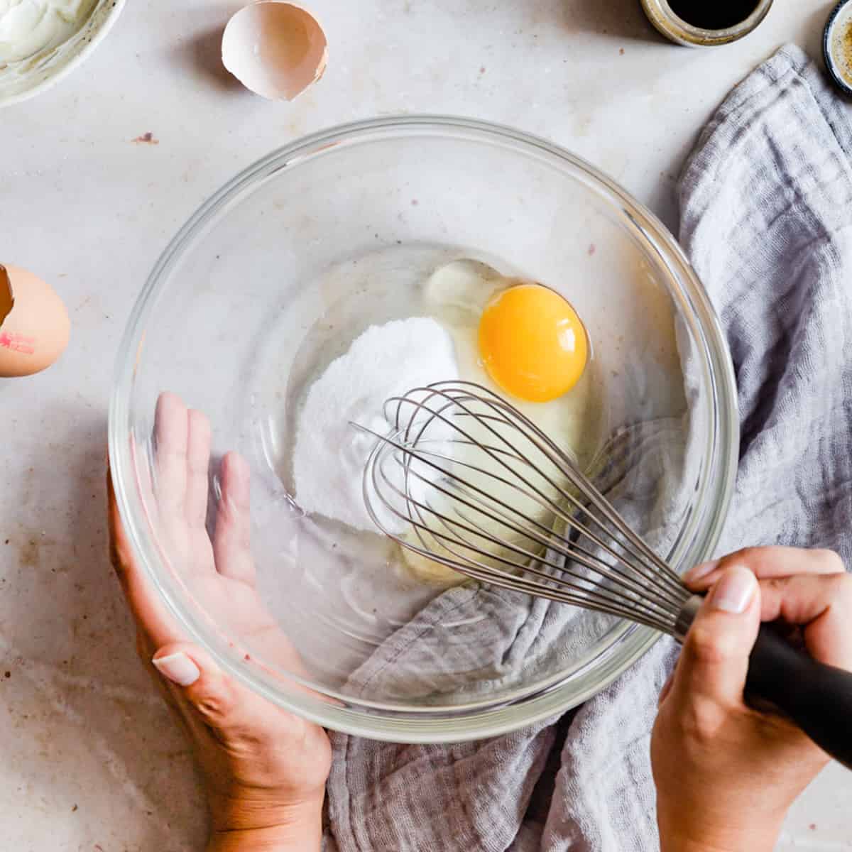 large glass mixing bowl with sugar and egg being whisked.