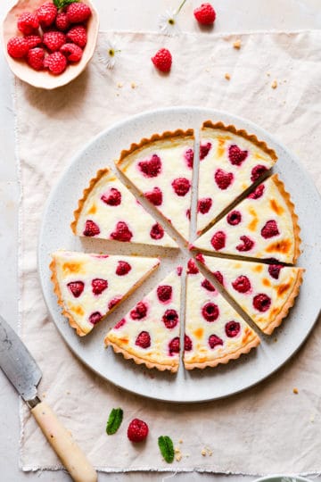 raspberry mascarpone tart cut into 8 slices with some fresh raspberries in a small bowl next to it.