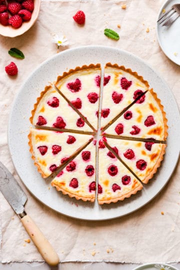 raspberry tart cut into 8 slices and resting on a large plate and pale pink kitchen towel.