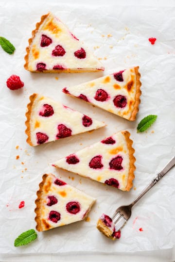 5 individual slices of raspberry mascarpone tart with one slice missing a bite and some fresh mint leaves around it.