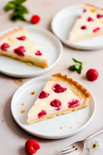 slice of raspberry tart on a plate with two more slices in the background.