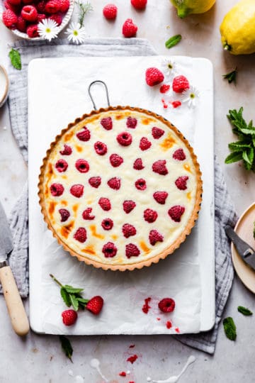 baked raspberry mascarpone tart on white chopping board and some fresh raspberries around it.