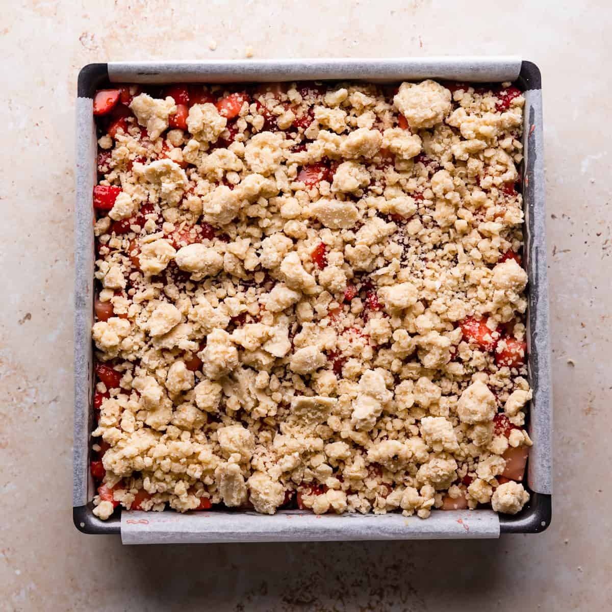 square baking tin with strawberry crumble topped with crumble mix.