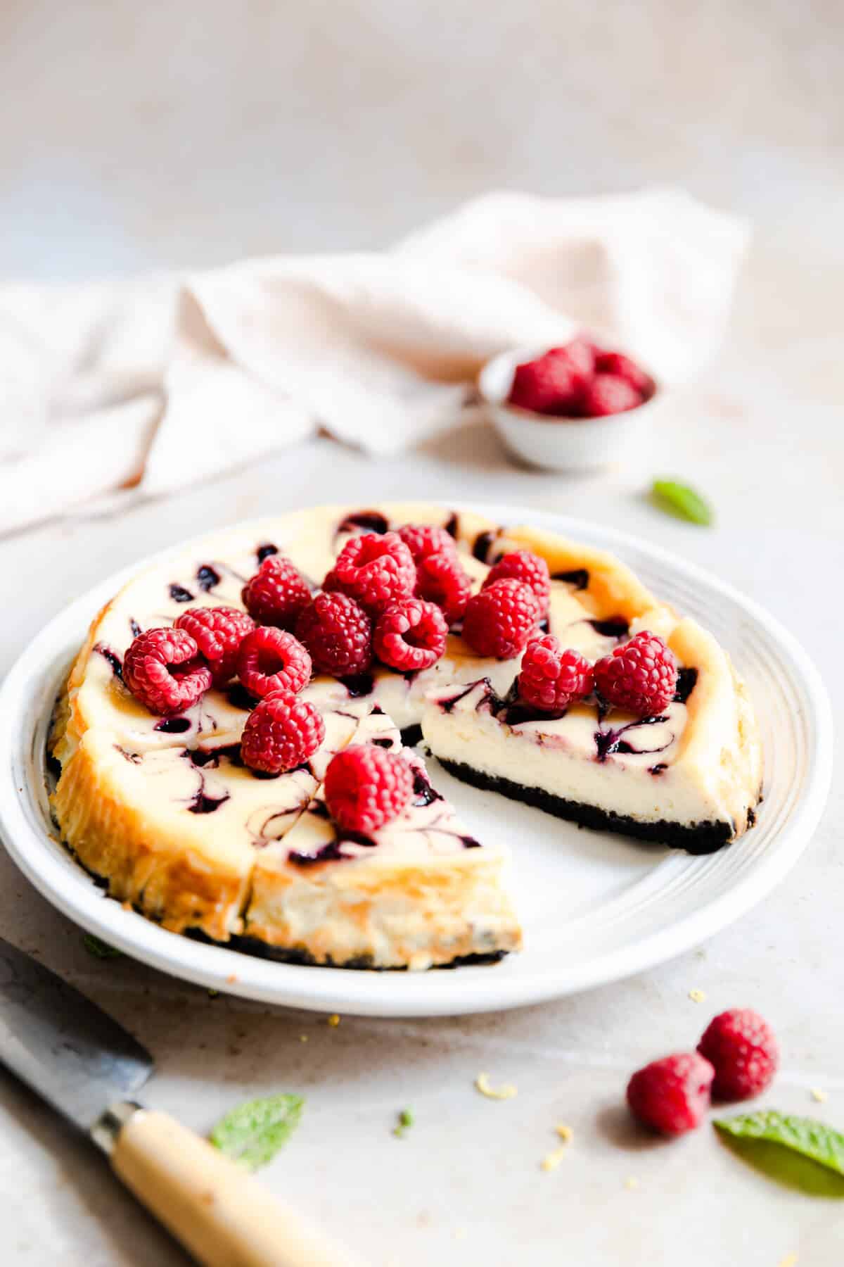 side angle of a raspberry ripple cheesecake on a white plate with a slice cut out