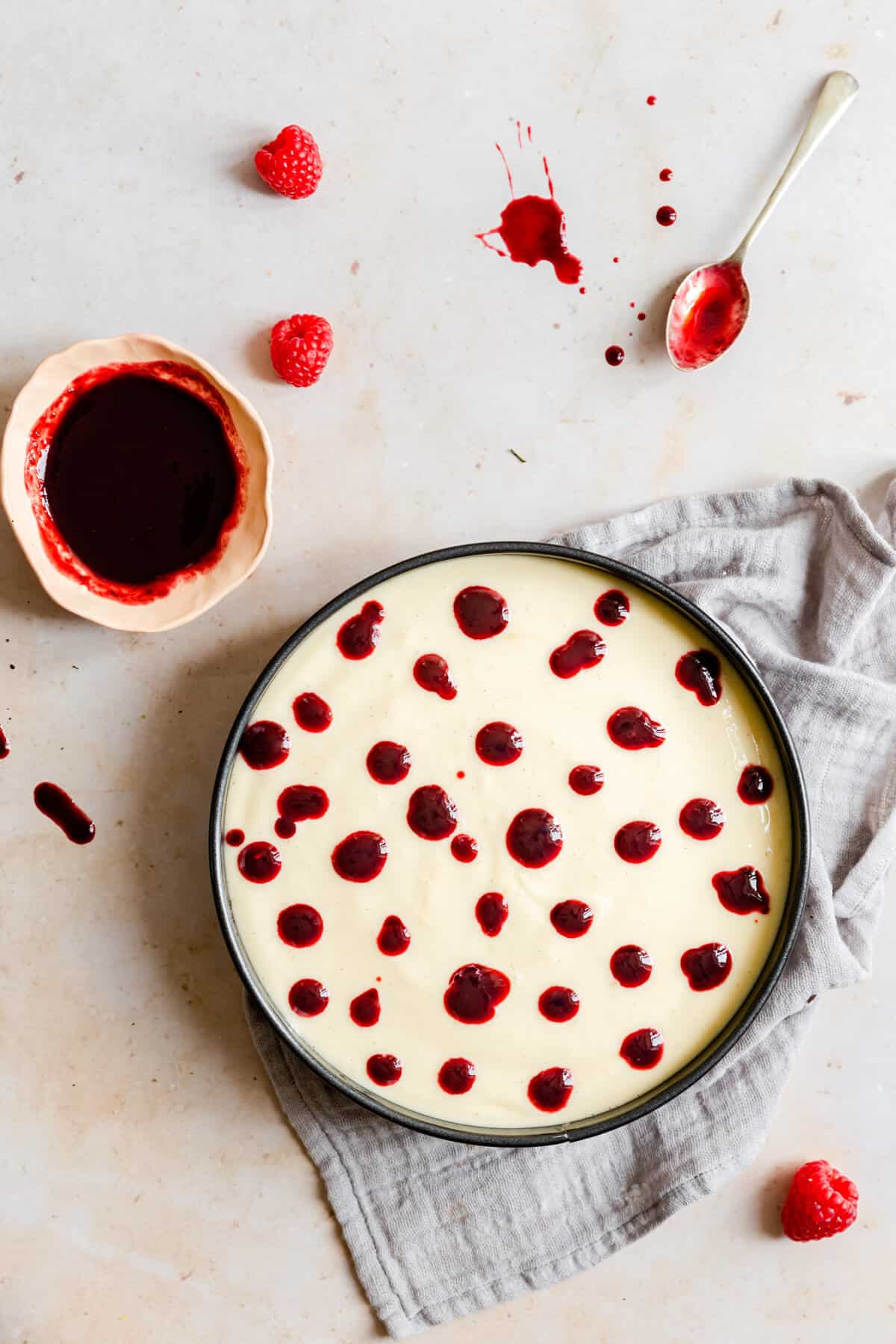 overhead shot of a cheesecake batter in a baking tin topped with raspberry sauce