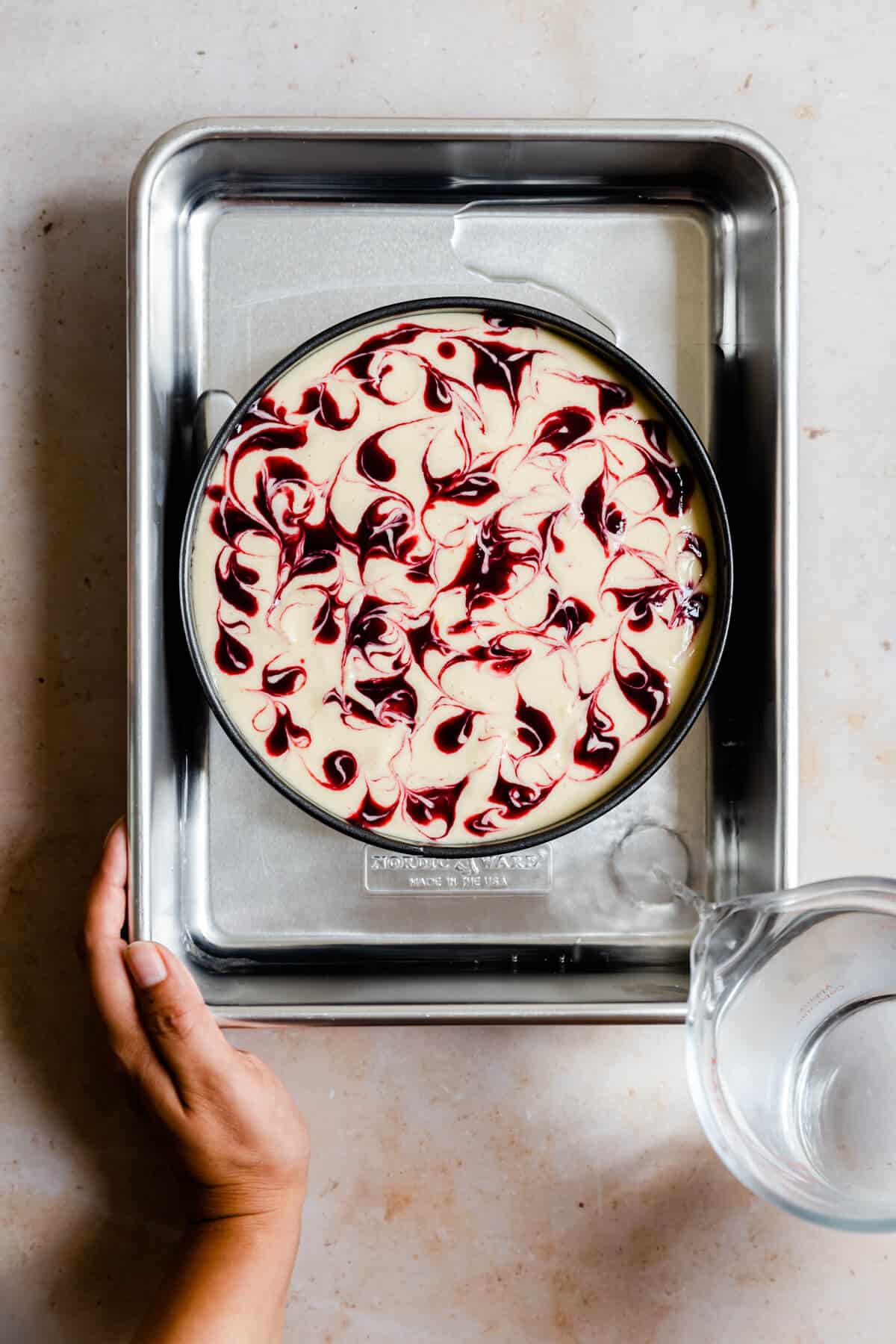 overhead shot of a person pouring water into water bath with cheesecake tin inside it
