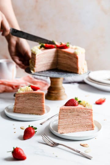 side shot of two slices of crepe cake and a person slicing the cake in the background