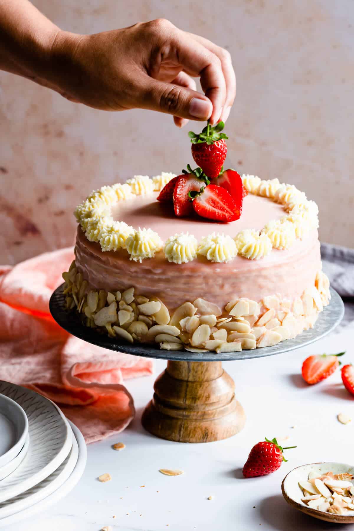 side shot of a hand lifting a strawberry from the top of the cake