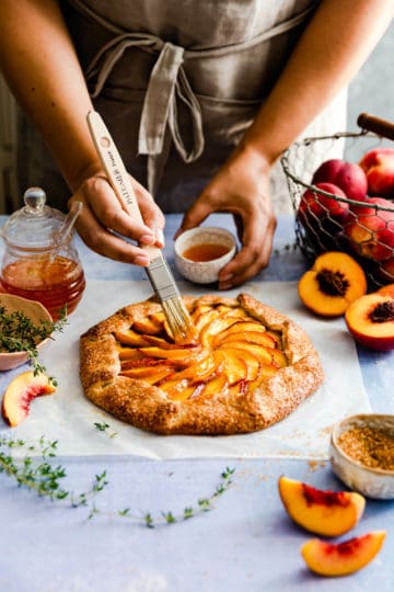 side view of person brushing some jam on top of peach galette