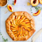 top view of baked peach galette with fresh thyme sprinkled on top