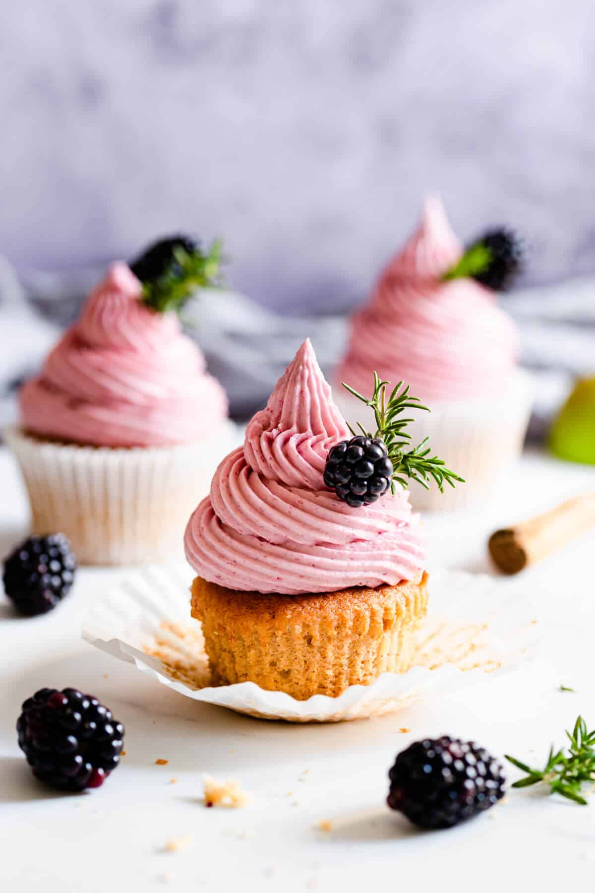 straight ahead shot of spiced apple and blackberry cupcake topped with fresh blackberry and rosemary