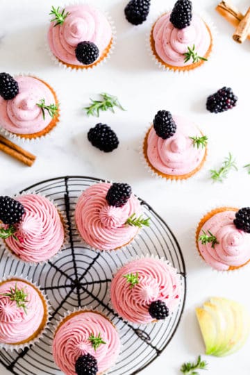 overhead shot of cupcakes topped with pink blackberry buttercream and fresh rosemary